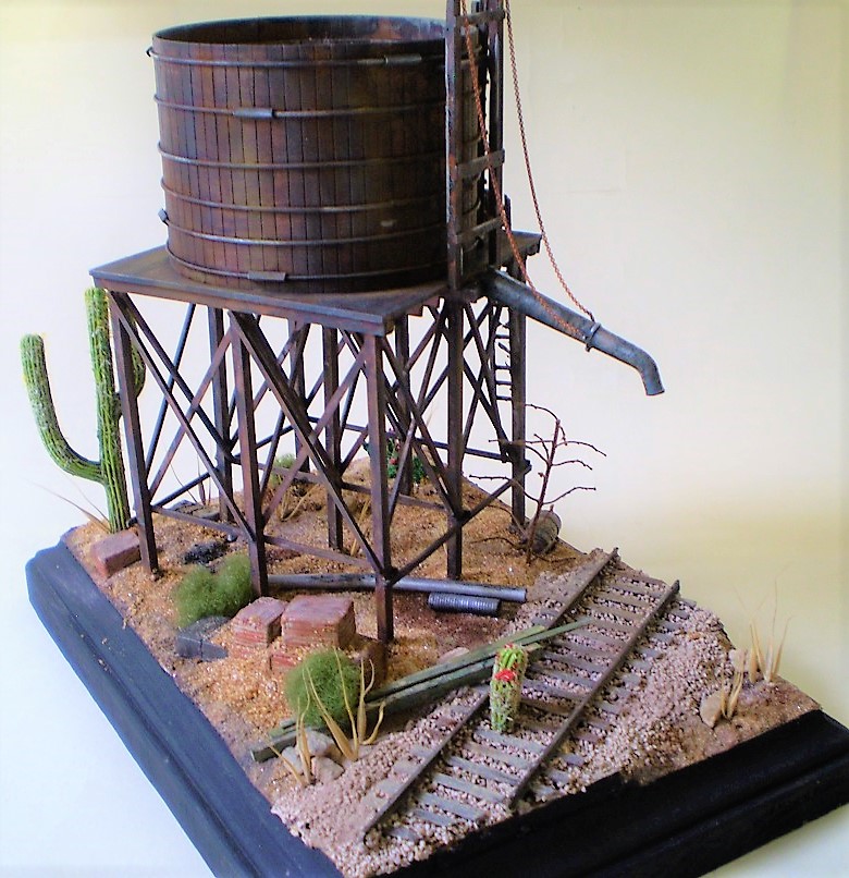 Water Tank (HO Scale)
This is an HO scale, old timey water tank from a forgotten manufacturer. Bits
and bobs from the spares box. The cacti are from Woodland Scenics.

Scale wood was added to the interior of the tank and I replaced the   
metal straps and turnbuckles around the exterior. Most of the dead   
foliage is from my yard.
