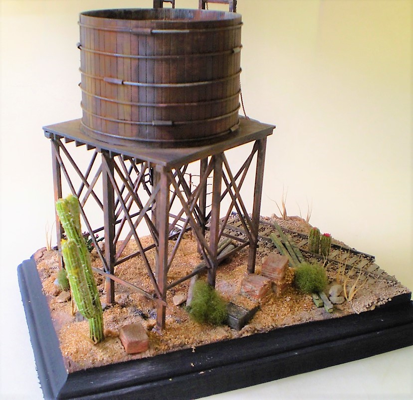 Water Tank (HO Scale)
This is an HO scale, old timey water tank from a forgotten manufacturer. Bits
and bobs from the spares box. The cacti are from Woodland Scenics.

Scale wood was added to the interior of the tank and I replaced the   
metal straps and turnbuckles around the exterior. Most of the dead   
foliage is from my yard.
