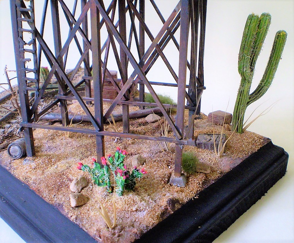 Water Tank (HO Scale)
This is an HO scale, old timey water tank from a forgotten manufacturer. Bits
and bobs from the spares box. The cacti are from Woodland Scenics.

Scale wood was added to the interior of the tank and I replaced the   
metal straps and turnbuckles around the exterior. Most of the dead   
foliage is from my yard.
